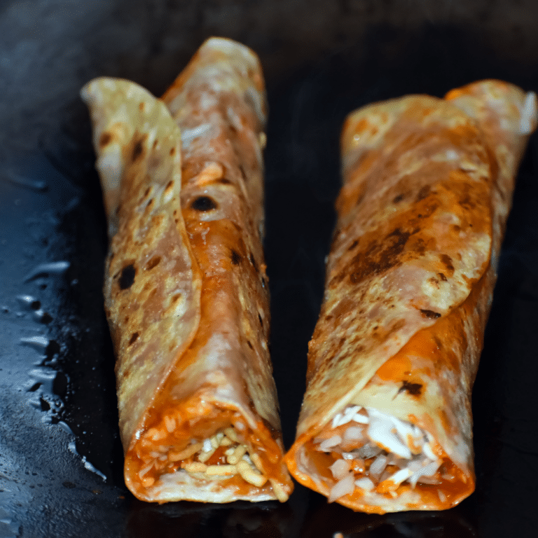 wo grilled frankie wraps sliced and served on a white plate, filled with vegetables and spiced paneer.