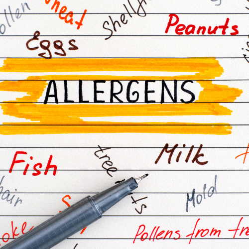 Handwritten list of common allergens such as peanuts, eggs, milk, and fish surrounding the word 'ALLERGENS' highlighted in yellow, with a pen nearby.