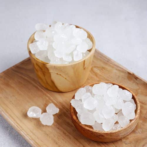 Two wooden bowls filled with white mishri (rock sugar) crystals on a wooden tray, showcasing their natural, irregular shapes and translucent texture